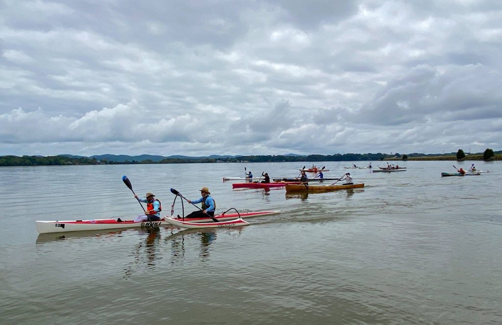 A Group Of People Rowing A Boat In A Body Of Water