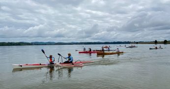 A Group Of People Rowing A Boat In A Body Of Water